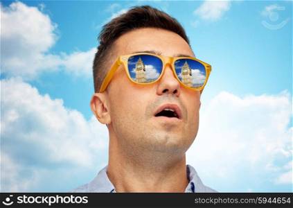 travel, tourism, sightseeing, emotions and people concept - face of man in sunglasses looking at big ben tower over blue sky and clouds background