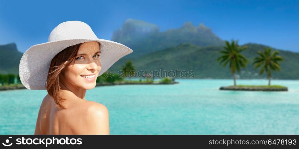 travel, tourism, summer holidays and vacation concept - happy young woman in sun hat at touristic resort over bora bora island beach background. happy woman in sun hat tanning on bora bora beach. happy woman in sun hat tanning on bora bora beach
