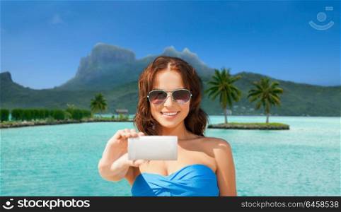 travel, tourism, summer holidays and vacation concept - happy young woman taking selfie by smartphone at touristic resort over bora bora island beach background. woman taking selfie by smartphone on bora bora