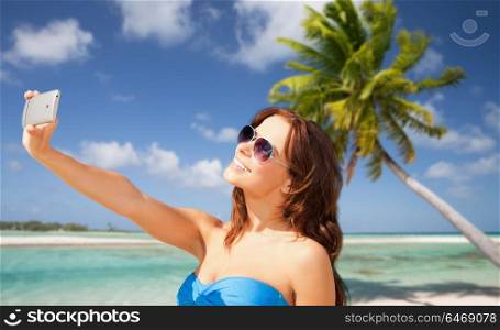 travel, tourism, summer holidays and vacation concept - happy young woman taking selfie by smartphone over exotic tropical beach with palm tree background. woman taking selfie by smartphone on beach