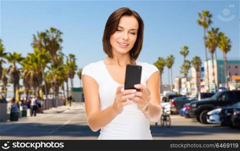 travel, tourism, summer holidays and vacation concept - happy young woman taking selfie by smartphone over venice beach in los angeles background. woman taking selfie by smartphone in los angeles