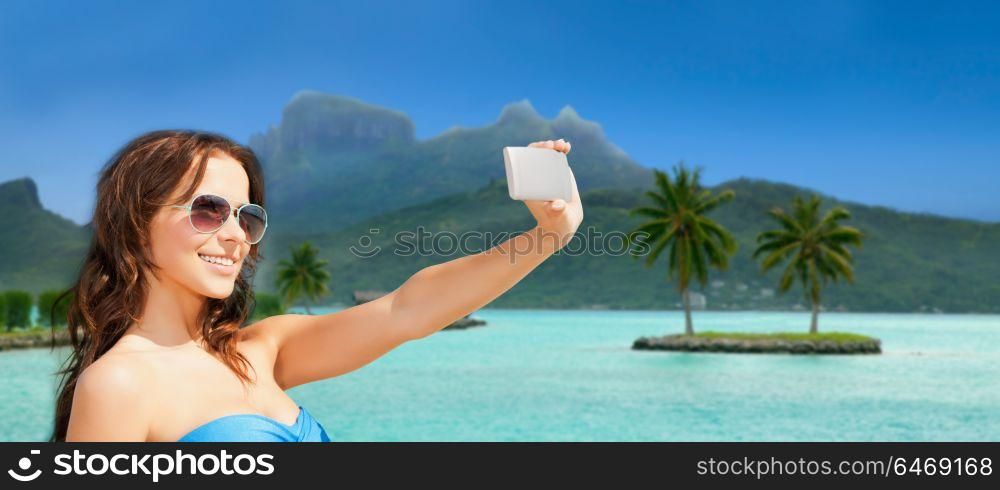 travel, tourism, summer holidays and vacation concept - happy young woman taking selfie by smartphone at touristic resort over bora bora island beach background. woman taking selfie by smartphone on bora bora