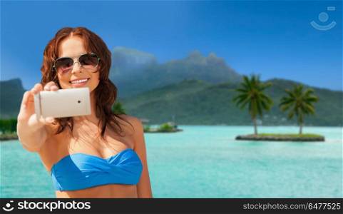 travel, tourism, summer holidays and vacation concept - happy young woman taking selfie by smartphone at touristic resort over bora bora island beach background. woman taking selfie by smartphone on bora bora. woman taking selfie by smartphone on bora bora