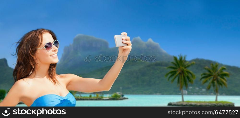 travel, tourism, summer holidays and vacation concept - happy young woman taking selfie by smartphone at touristic resort over bora bora island beach background. woman taking selfie by smartphone on bora bora. woman taking selfie by smartphone on bora bora