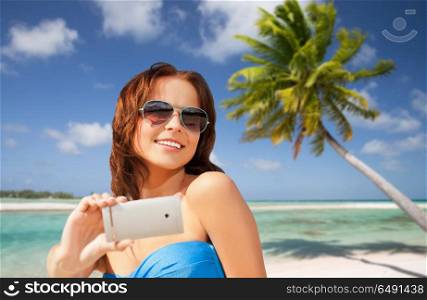 travel, tourism, summer holidays and vacation concept - happy young woman taking selfie by smartphone over exotic tropical beach with palm tree background in french polynesia. woman taking selfie by smartphone on beach. woman taking selfie by smartphone on beach