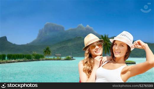 travel, tourism, summer holidays and vacation concept - smiling young women in hats at touristic resort over exotic bora bora island beach background. smiling young women in hats on bora bora beach