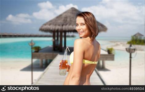 travel, tourism, summer holidays, vacation and people concept - happy beautiful woman with bottle of drink and straw over exotic tropical beach with bungalow shed background. happy woman with bottle of drink on summer beach