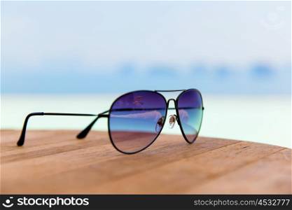 travel, tourism, summer vacation and fashon accessories concept - shades or sunglasses on table at beach
