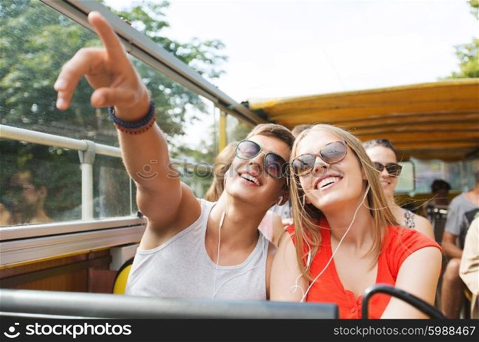 travel, tourism, summer vacation, sightseeing and people concept - happy teenage couple in sunglasses traveling by tour bus and listening to music with earphones