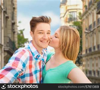 travel, tourism, summer vacation, technology and love concept - happy couple taking selfie with smartphone or camera and kissing over city street background
