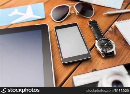 travel, tourism, technology and objects concept - close up of smartphone with tablet pc computer, airplane ticket and personal stuff