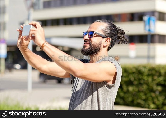travel, tourism, technology and people concept - smiling man taking video or selfie by smartphone on summer city street