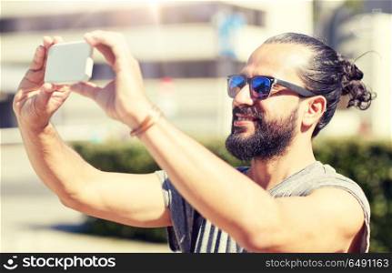 travel, tourism, technology and people concept - smiling man taking video or selfie by smartphone on summer city street. man taking video or selfie by smartphone in city. man taking video or selfie by smartphone in city