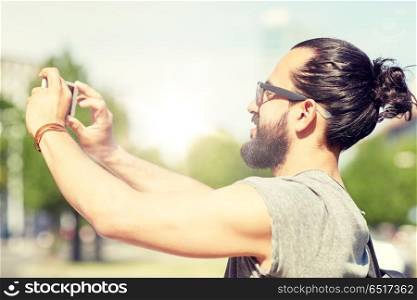travel, tourism, technology and people concept - smiling man taking video or selfie by smartphone on summer city street. man taking video or selfie by smartphone in city. man taking video or selfie by smartphone in city