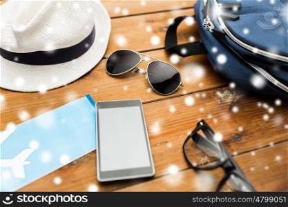travel, tourism, technology and winter holidays concept - smartphone, airplane ticket and traveler personal stuff over snow