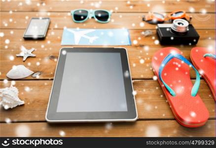 travel, tourism, technology and winter holidays concept - tablet pc computer, airplane ticket and beach stuff over snow