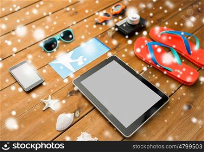 travel, tourism, technology and winter holidays concept - tablet pc computer, airplane ticket and beach stuff over snow