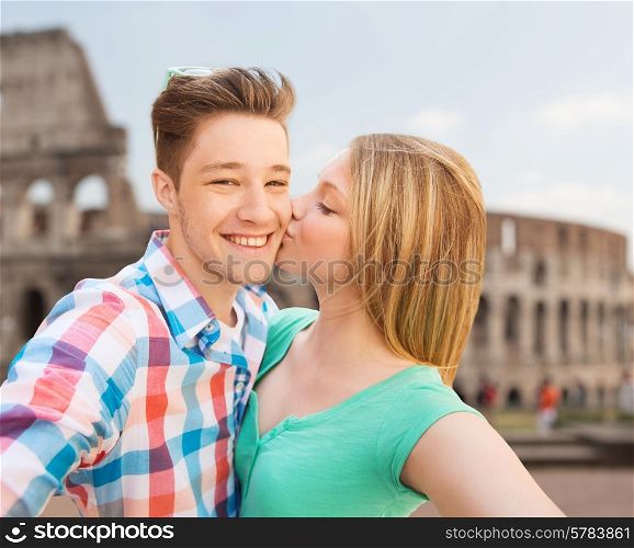 travel, tourism, technology, love and people concept - smiling couple kissing and taking selfie over coliseum background