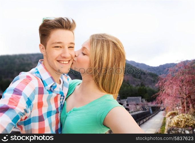 travel, tourism, technology, love and people concept - smiling couple kissing and taking selfie over asian village landscape background