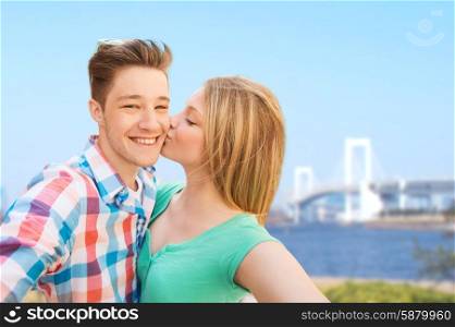 travel, tourism, technology, love and people concept - smiling couple kissing and taking selfie over rainbow bridge in tokyo and river background