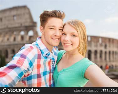 travel, tourism, technology, people and love concept - smiling couple with smartphone or camera taking selfie over coliseum background