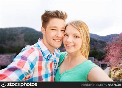 travel, tourism, technology, people and love concept - smiling couple with smartphone or camera taking selfie over asian village landscape background
