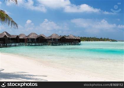 travel, tourism, vacation and summer holidays concept - bungalow huts in sea water on exotic resort beach