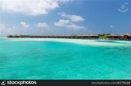 travel, tourism, vacation and summer holidays concept - bungalow huts in sea water on exotic resort beach