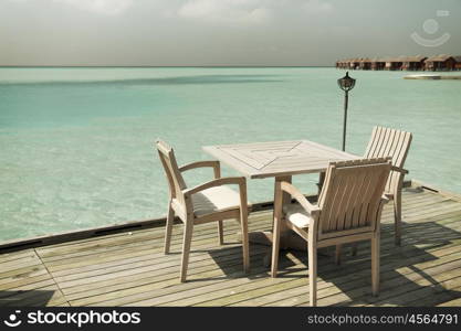 travel, tourism, vacation and summer holidays concept - outdoor restaurant wooden terrace with table and chairs over sea background