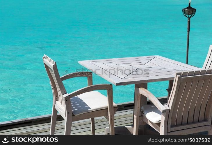 travel, tourism, vacation and summer holidays concept - outdoor restaurant wooden terrace with table and chairs over sea background. table and chairs at restaurant terrace over sea
