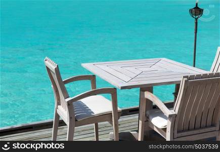 travel, tourism, vacation and summer holidays concept - outdoor restaurant wooden terrace with table and chairs over sea background. table and chairs at restaurant terrace over sea