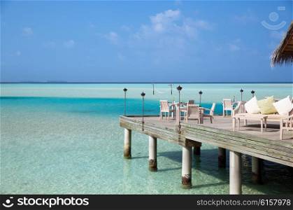 travel, tourism, vacation and summer holidays concept - outdoor restaurant wooden terrace with table and chairs over sea background