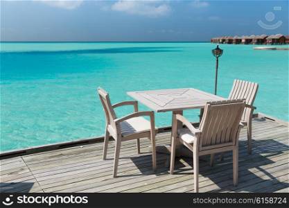 travel, tourism, vacation and summer holidays concept - outdoor restaurant wooden terrace with table and chairs over sea background