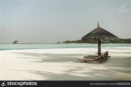 travel, tourism, vacation and summer holidays concept - palapa and sunbeds over sea and sky on maldives beach