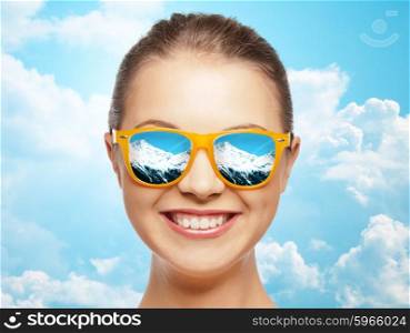 travel, tourism, winter resort and people concept - happy face of teenage girl in sunglasses with mountains reflection over blue sky and clouds background
