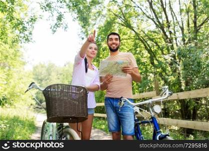 travel, trip, leisure and lifestyle concept - happy young couple with map and bicycles looking for location at country in summer. couple with map and bicycles at country in summer