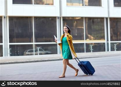 travel, trip, tourism, people and vacation concept - happy young woman with carry-on travel bag and map walking along city street