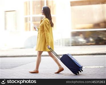 travel, trip, tourism, people and vacation concept - happy young woman with carry-on travel bag and map walking along city street