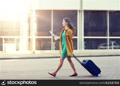 travel, trip, tourism, people and vacation concept - happy young woman with carry-on travel bag and map walking along city street. happy young woman with travel bag and map in city