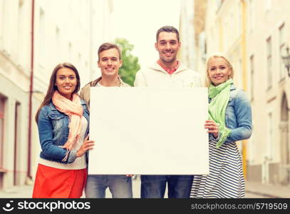 travel, vacation and advertising concept - group of smiling friends with blank white board in the city