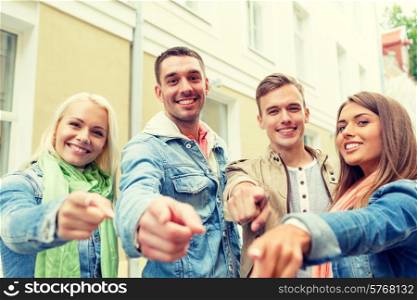 travel, vacation and friendship concept - group of smiling friends in city pointing finger at you