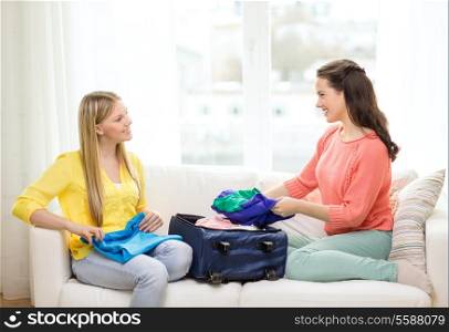 travel, vacation and friendship concept - two smiling teenage girls packing suitcase at home
