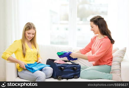 travel, vacation and friendship concept - two smiling teenage girls packing suitcase at home