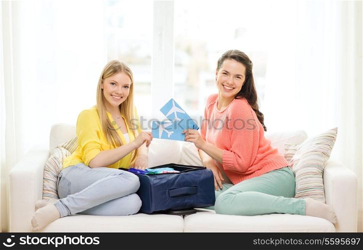 travel, vacation and friendship concept - two smiling teenage girls with plane tickets and packed suitcase