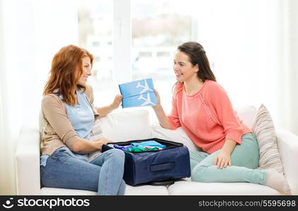 travel, vacation and friendship concept - two smiling teenage girls with plane tickets and packed suitcase