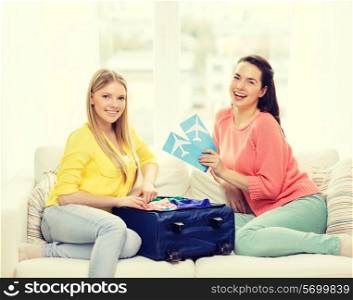 travel, vacation and friendship concept - two smiling teenage girls with plane tickets and packed suitcase