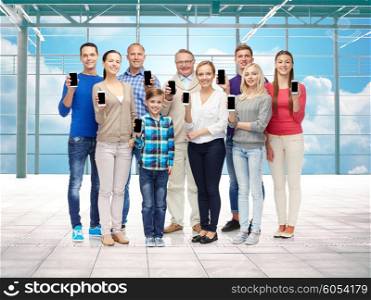 travel, vacation and people concept - group of happy people or big family showing smartphones over airport terminal window and sky background