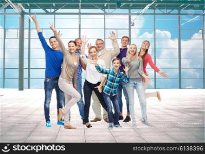 travel, vacation and people concept - group of happy people or big family having fun and waving hands over airport terminal window and sky background