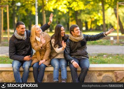 travel, vacation, people, gesture and friendship concept - group of smiling friends waving hands in city park