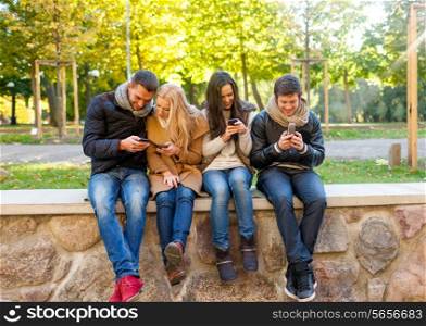 travel, vacation, people, technology and friendship concept - group of smiling friends with smartphones in city park